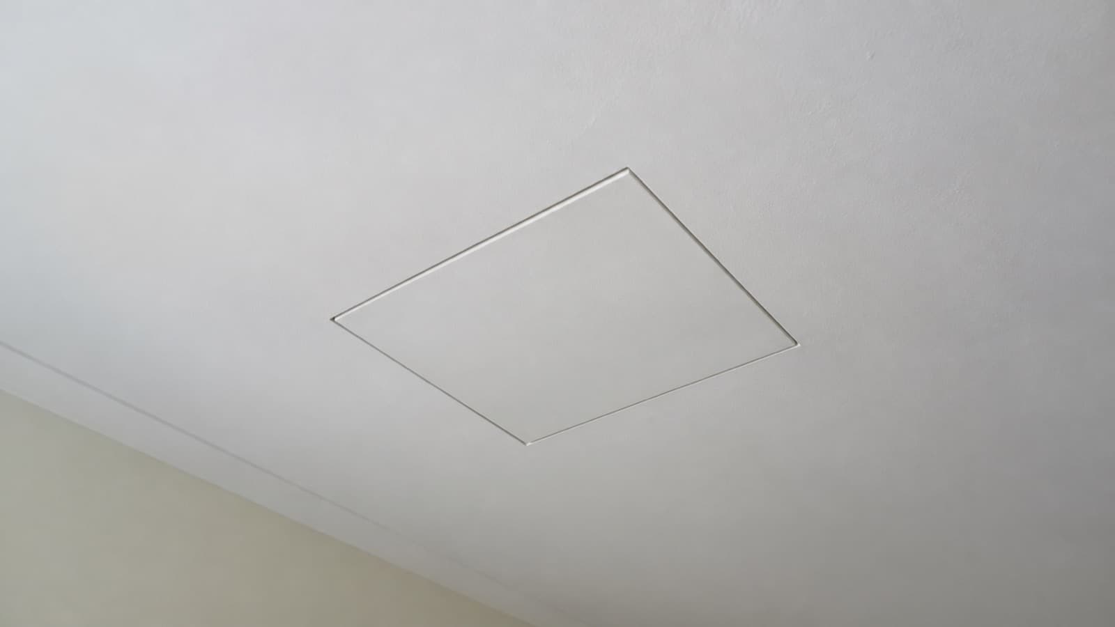 A closed square access hatch set into a plain painted ceiling.